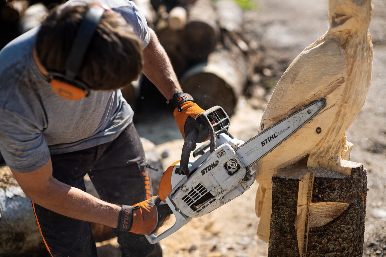 Mężczyzna w nausznikach ochronnych wycina orła z drewna benzynową pilarką łańcuchową STIHL MS 193 C-E z osprzętem do carvingu
